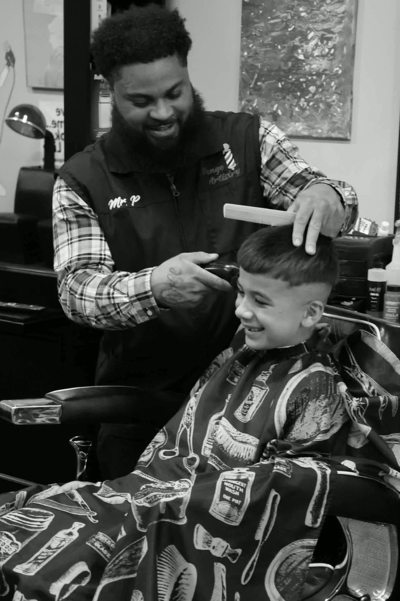 Mr. P smiling while cutting a young client's hair in his barber chair